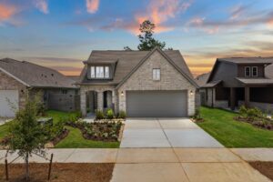 A two-story brick house with a double garage, landscaped front yard, and driveway, surrounded by neighboring homes at sunset.